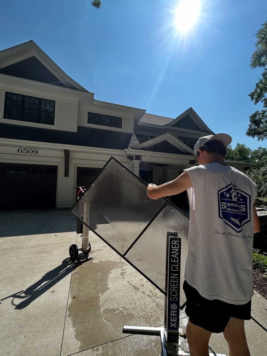 Man using a Xero screen cleaner in front of a modern home on a sunny day.
