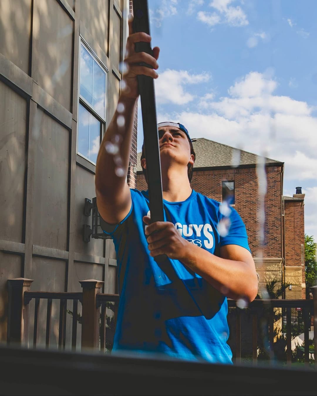 Young man in a blue t-shirt cleaning a window with a squeegee on a sunny day.