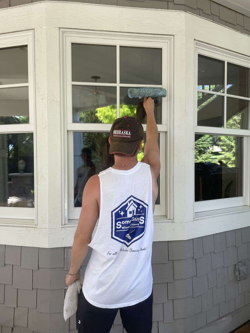 Man cleaning windows with a squeegee, wearing a sleeveless shirt and baseball cap.