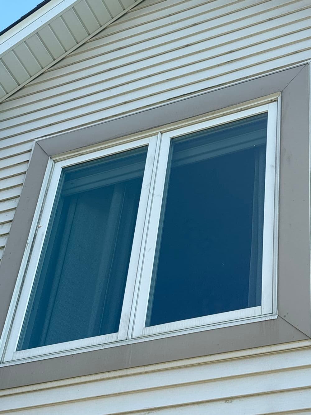 Double window on a residential house with white siding and beige trim.