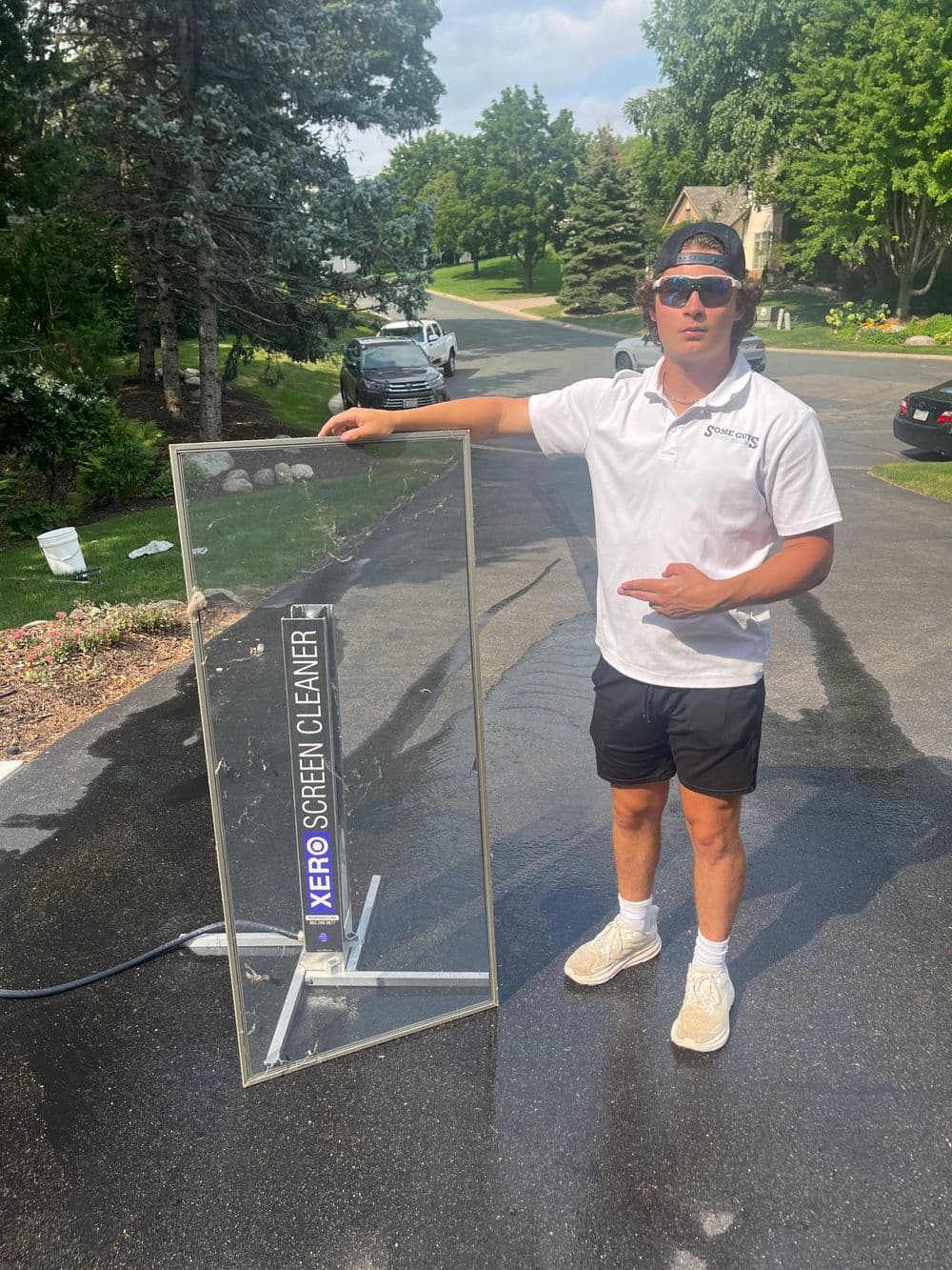 Man demonstrating Xero screen cleaner next to a clear glass panel in a residential setting.
