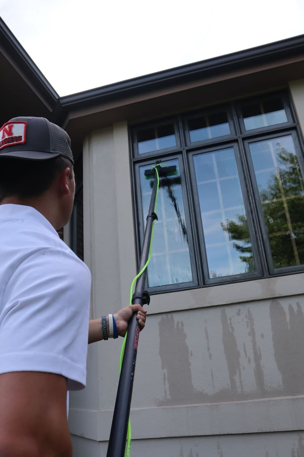 Person using a window cleaning pole to clean large residential windows outdoors.