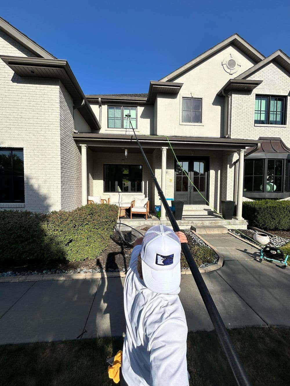Person cleaning a home's second-story window with a long pole from the front yard.