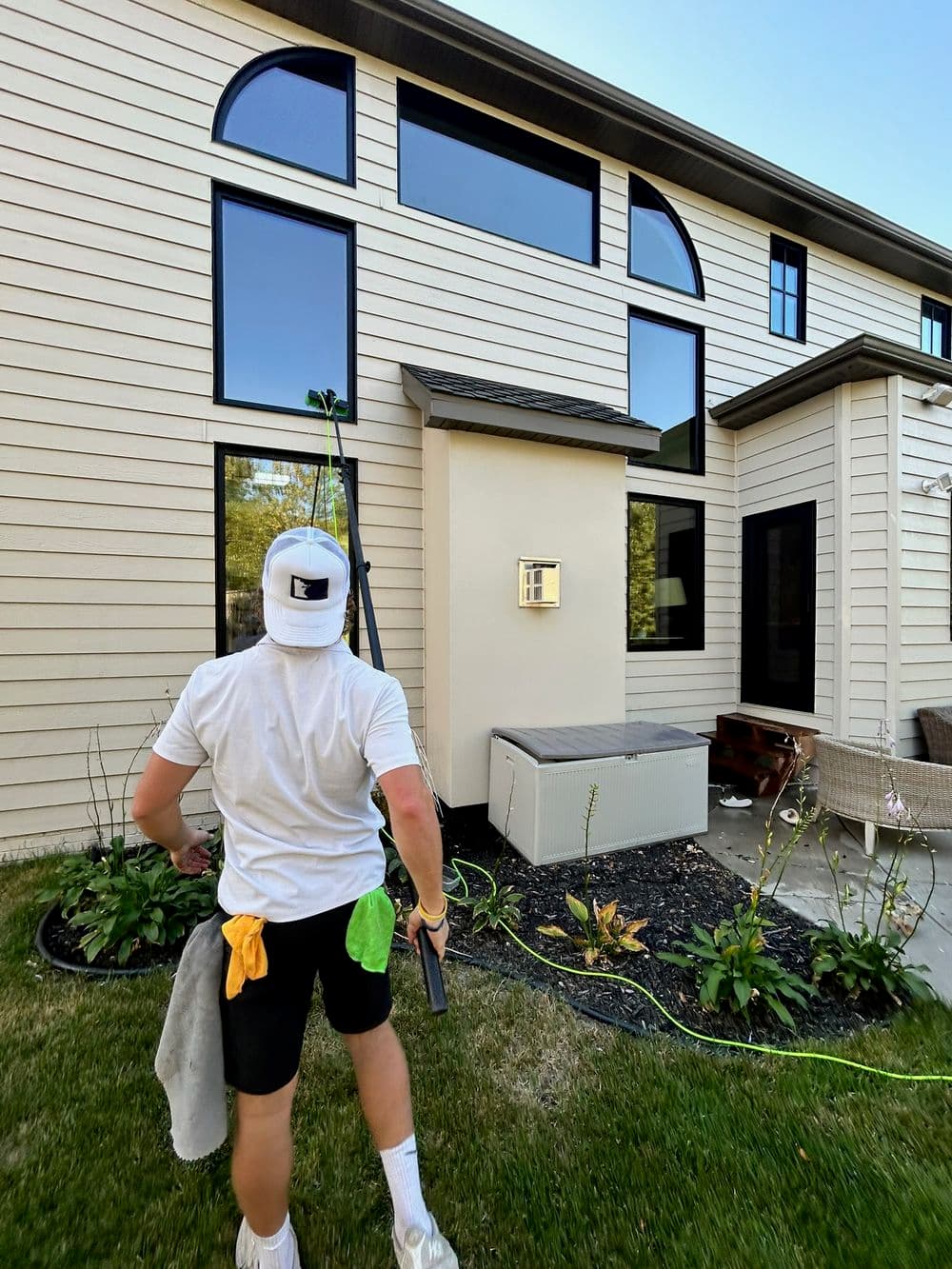 Man cleaning windows of a modern house with a green squeegee and towel in hand.