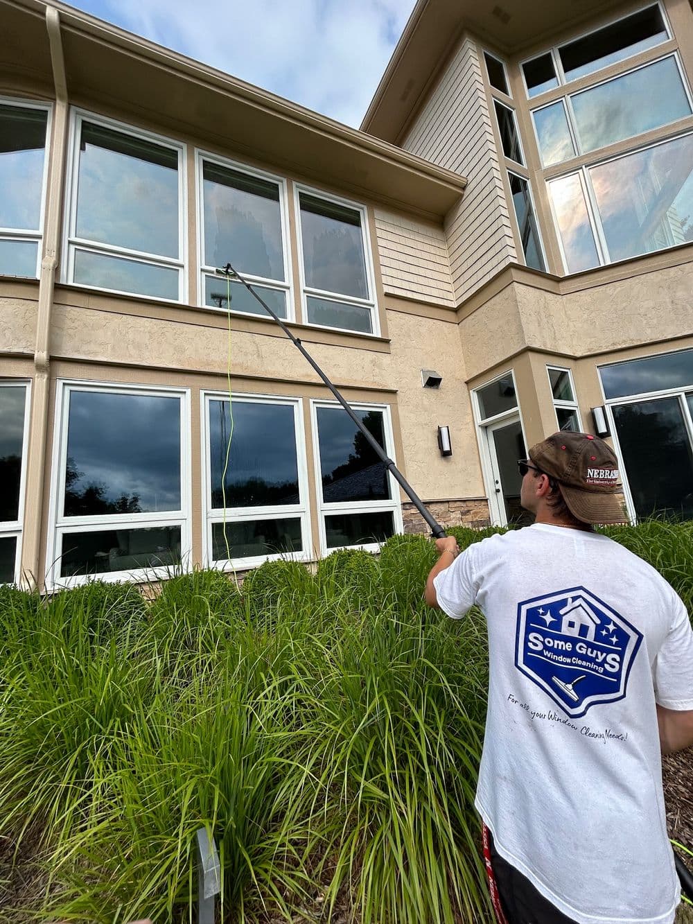 Window cleaning professional using a pole to wash high windows on a modern home exterior.