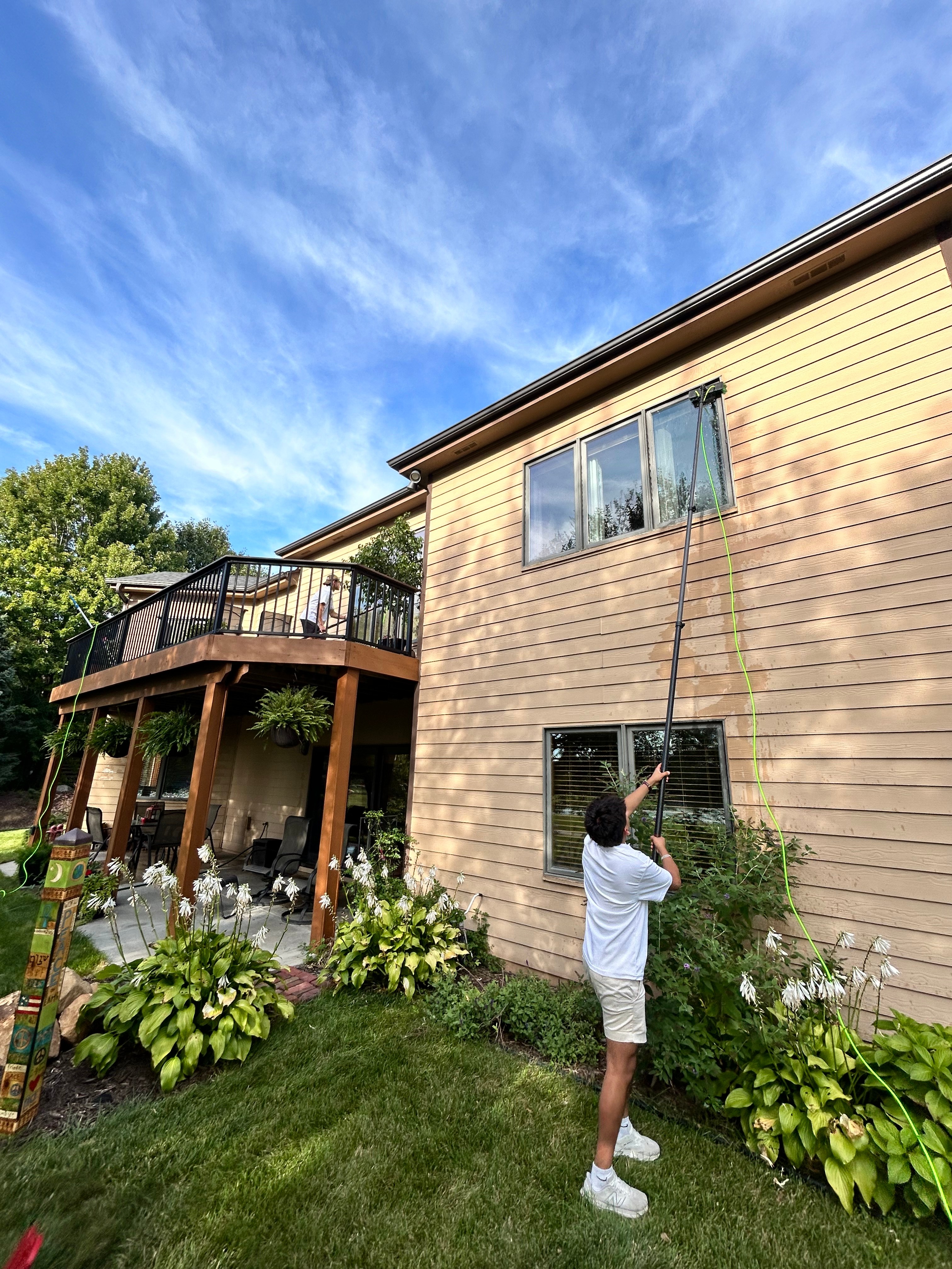 Window cleaning technician reaching second floor windows at sunset with beautiful Minnesota backyard